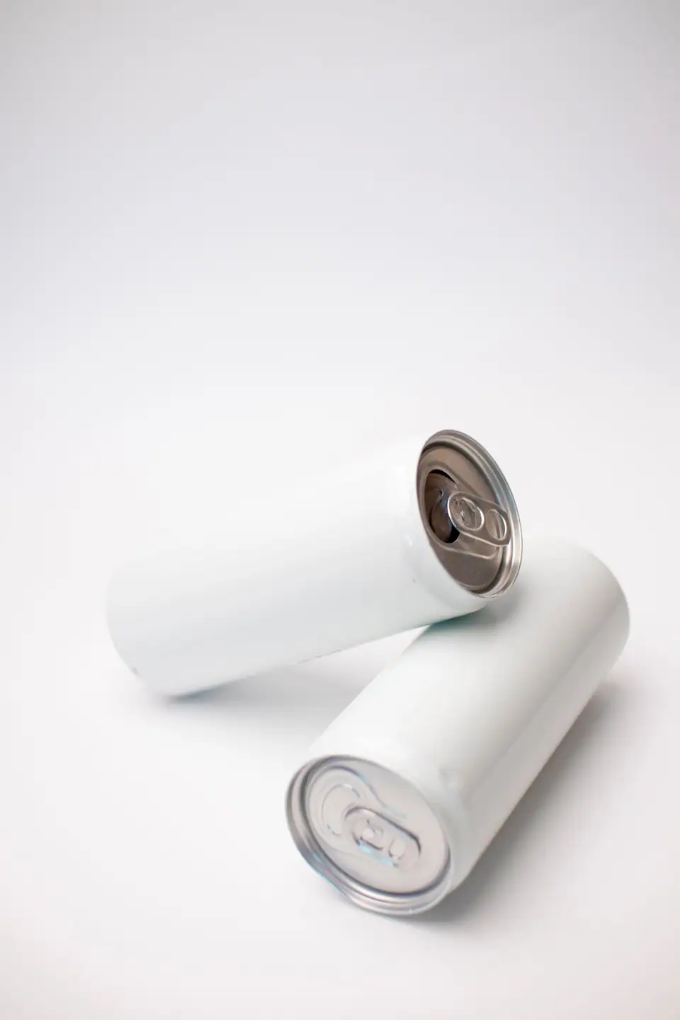 Two plain white aluminum beverage cans with no labels lying on a white surface