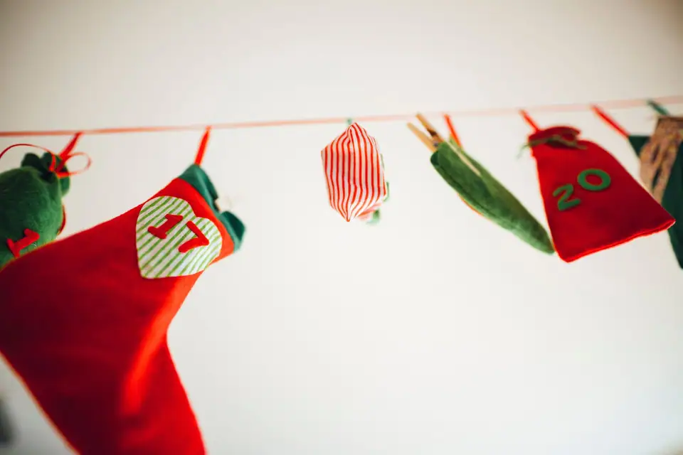 A felt advent calendar of small stockings and pouches with number patches hanging from a red string