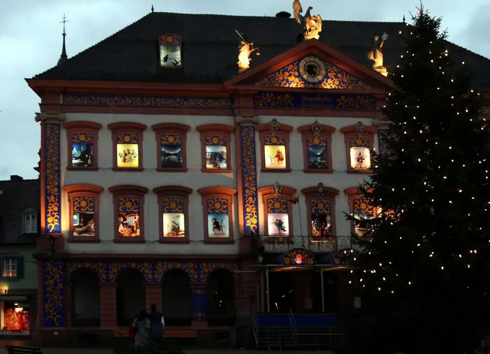 The town hall in Gengenbach, Germany, lit at dusk with its windows turned into a giant outdoor advent calendar beside a Christmas tree