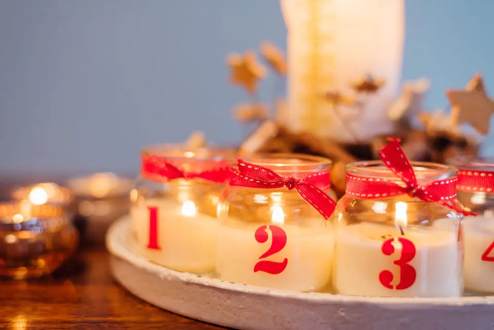 Lit candles in glass jars numbered 1, 2 and 3 with red ribbons on a round wooden tray