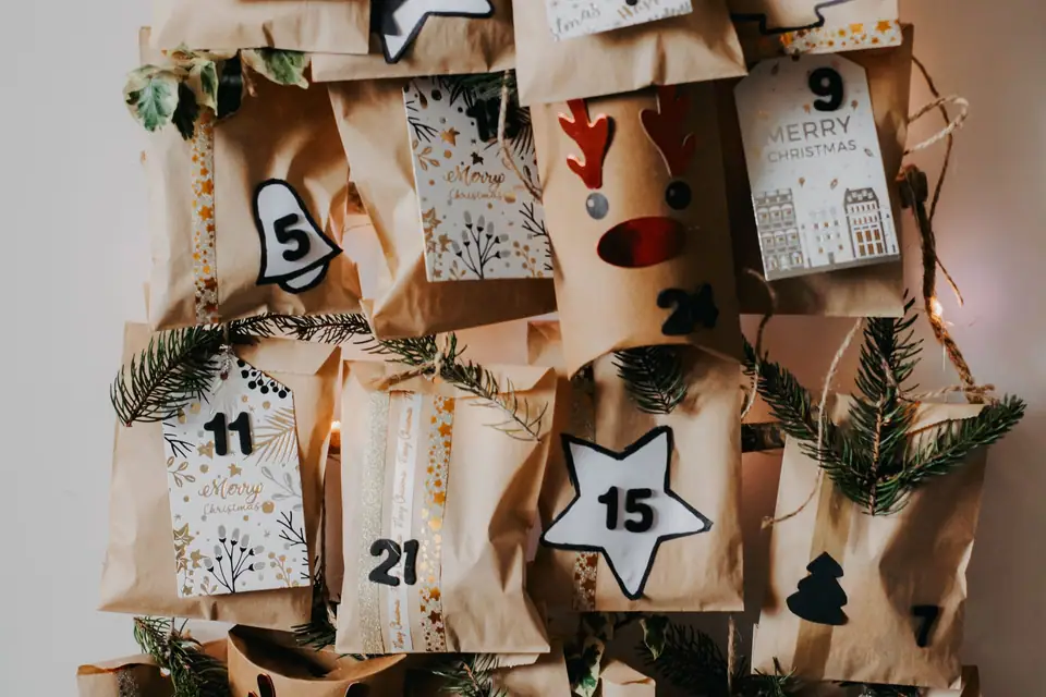 A homemade advent calendar of brown paper bags with number tags, stars and pine sprigs