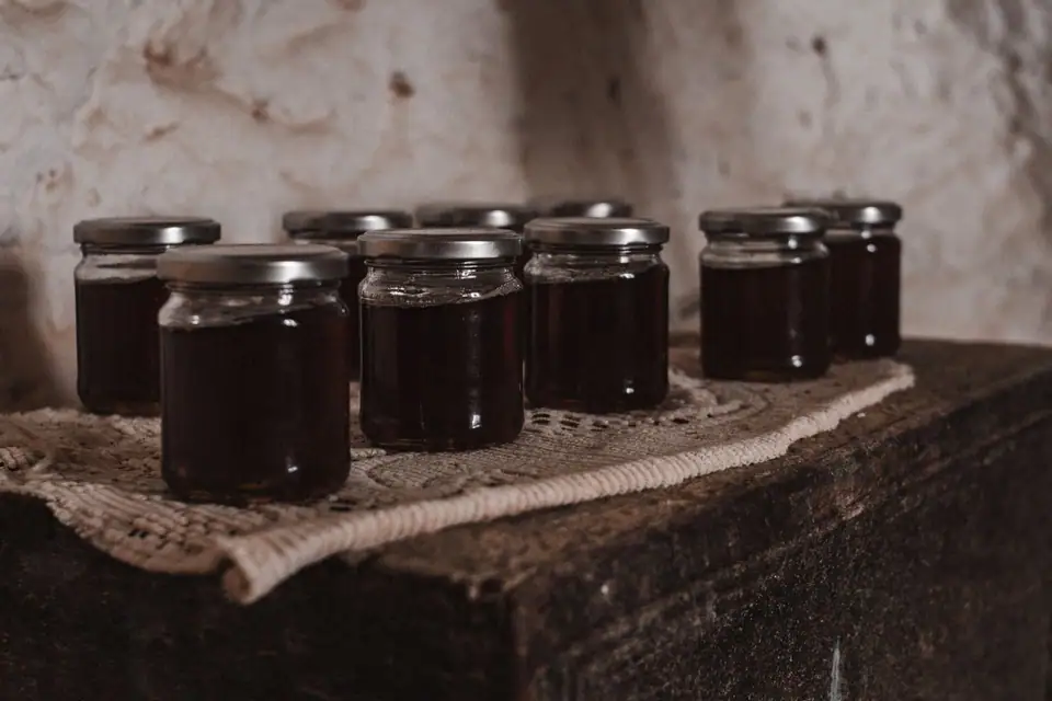Rows of small glass jars of dark fruit preserves on a wooden surface